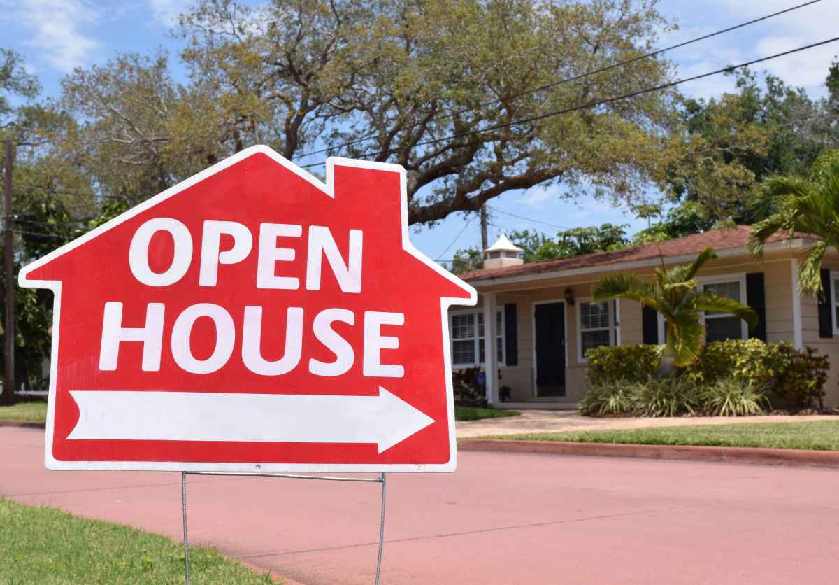 A red open house sign pointing to a house.