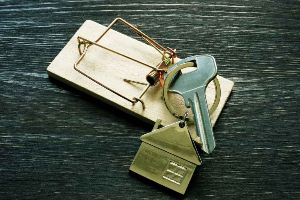 A house key is caught in a mousetrap, signifying a real estate scam. 