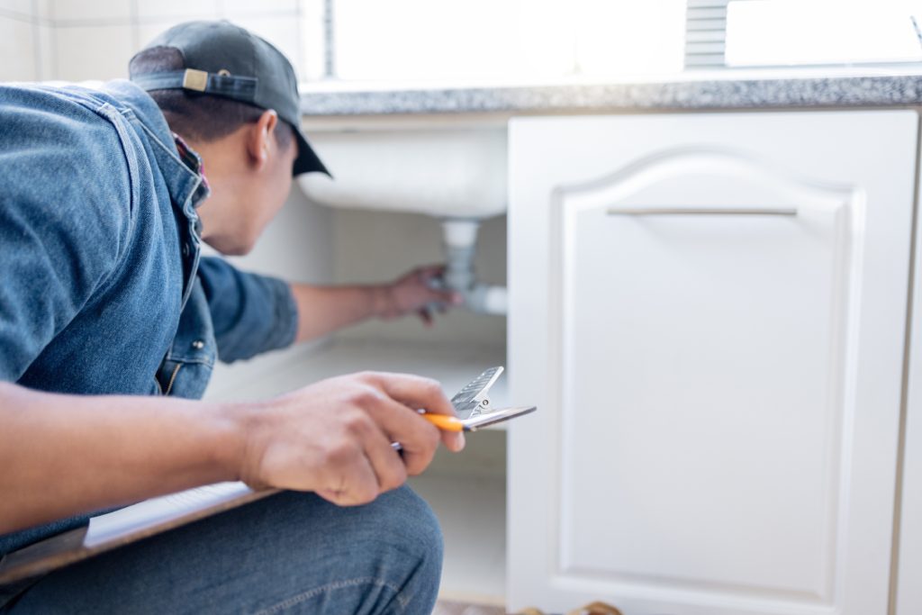 A home inspector looking at the pipes under a sink 