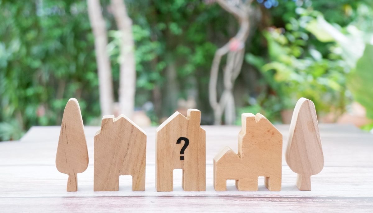 Wooden house-shaped blocks aligned between tree blocks, one home block has a question mark on it.