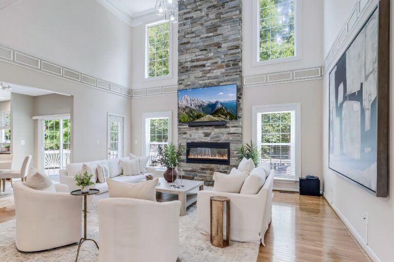 After staging: family room at 3985 Fawnridge Ct with light, scaled seating facing the two-story stone fireplace