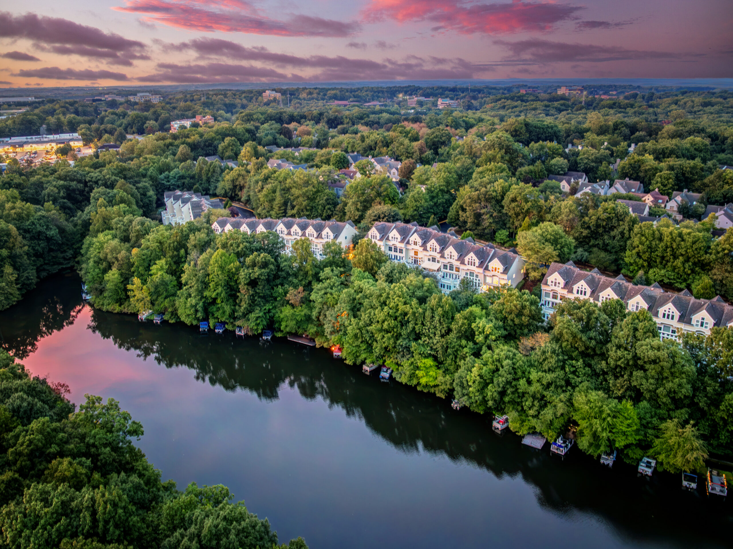 Aerial view of townhomes beside a lake surrounded by trees at sunset
