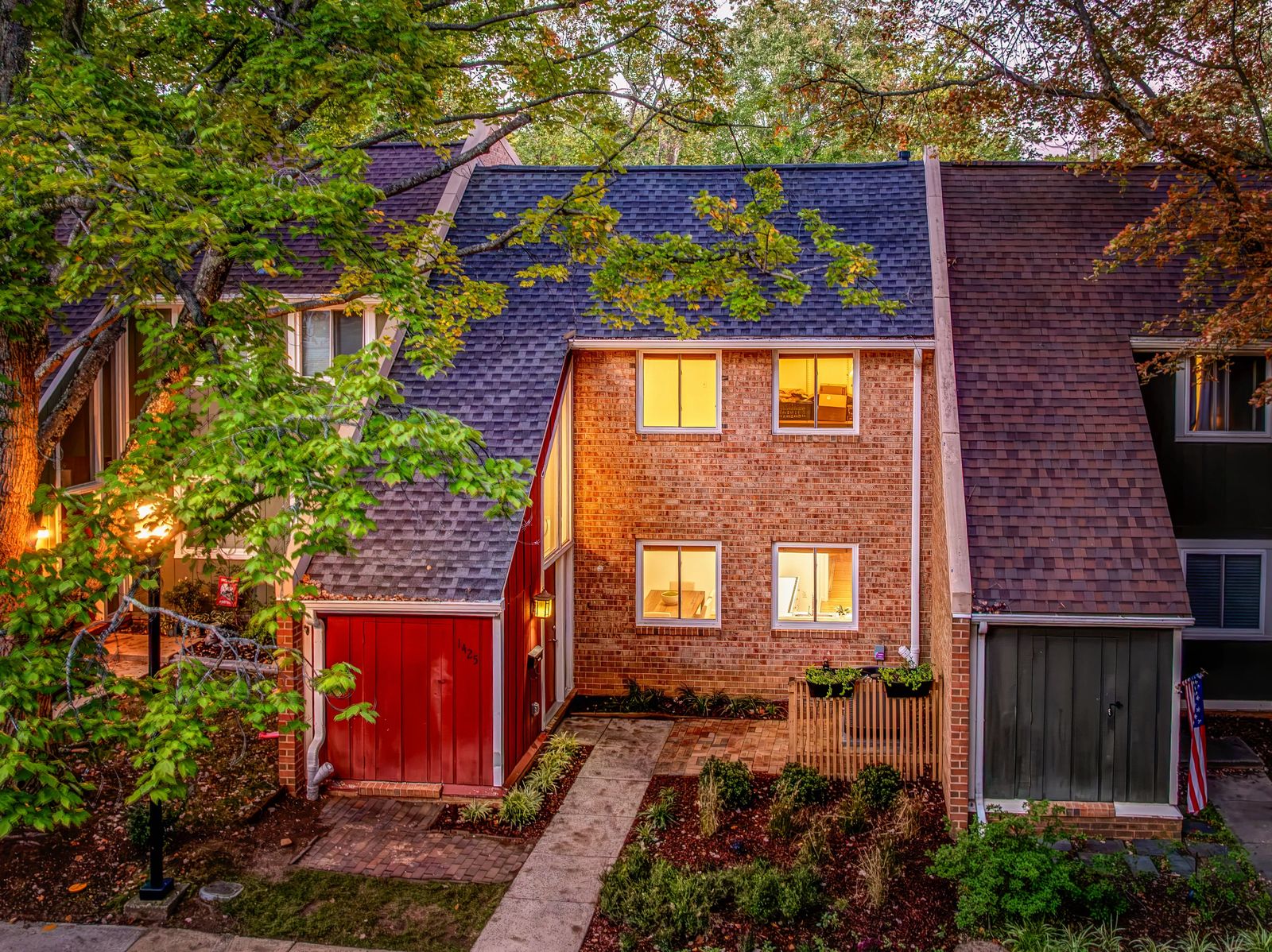 Brick townhome in the Forest Edge cluster of Reston VA at dusk, with a red front gate and landscaped walk