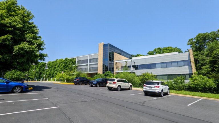Three-story glass and stone office building with a vine-covered facade, surrounded by tall trees, with cars in the parking lot in front, at the Lake Fairfax Business Center in Reston VA