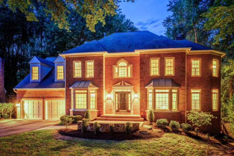 Brick colonial with a two-car garage on a wooded lot in North Reston VA at dusk