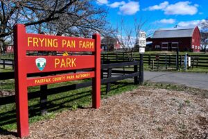 Entrance sign for Frying Pan Farm Park, a Fairfax County Park Authority site in Herndon, Virginia, with a red barn in the background
