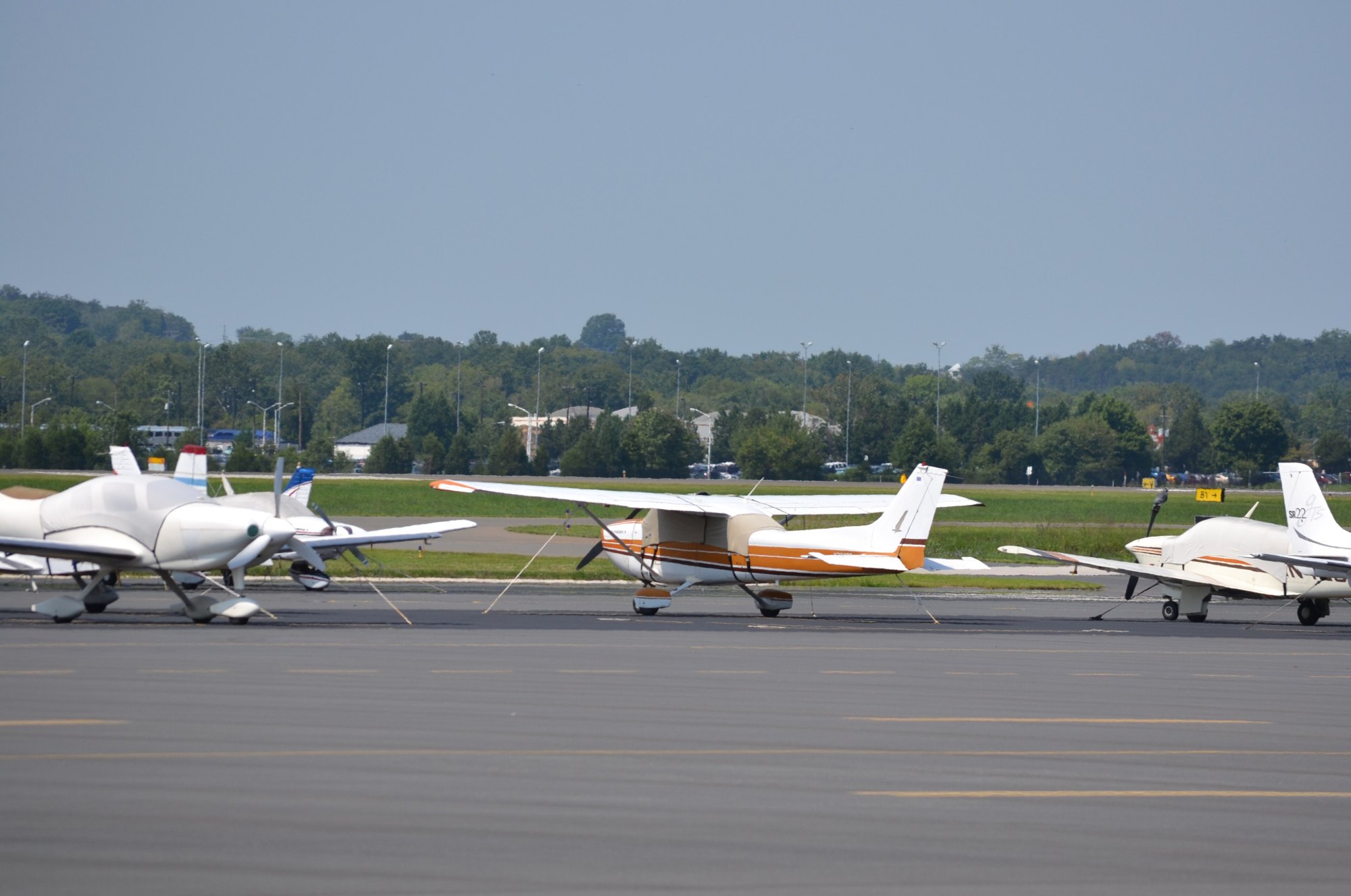 Several small single-engine and twin-engine propeller planes parked on the ramp at Manassas Regional Airport with trees in the background, Manassas VA